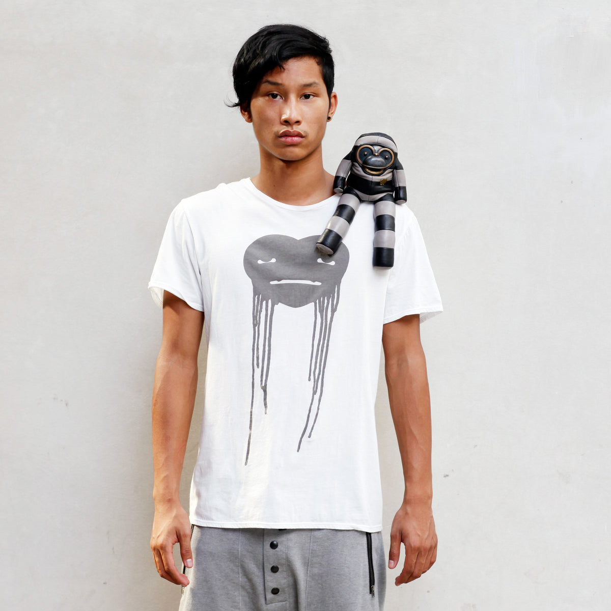 Person wearing a white t-shirt with a graphic design and a striped figurine sitting on their shoulder