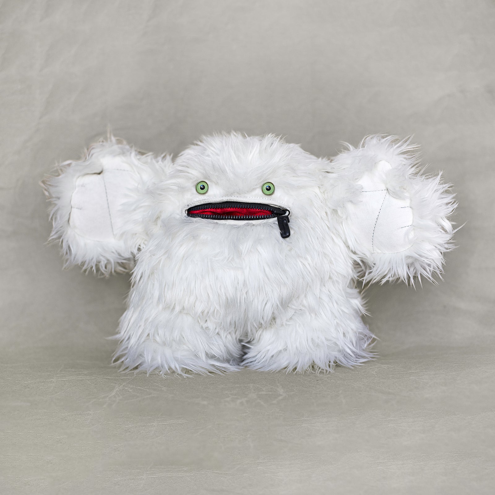 White fluffy creature with a black and red zipper mouth on a gray background