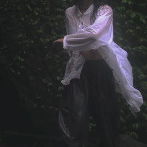 Person in a white button up shirt and black pants spinning with their arms outstretched in the rain 