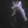 Person in a white button up shirt and black pants spinning with their arms outstretched in the rain 