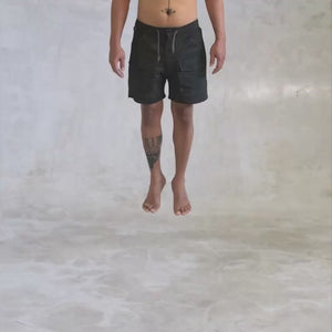 person from the waist down wearing black cargo shorts spinning in the air against a light gray background 