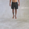 person from the waist down wearing black cargo shorts spinning in the air against a light gray background 