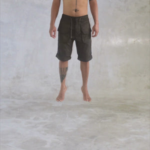 Person from the waist down wearing black mid length cargo shorts spinning round in the air against a gray textured background