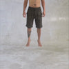 Person from the waist down wearing black mid length cargo shorts spinning round in the air against a gray textured background