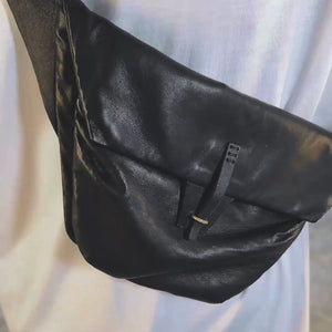 Person in a white shirt showing all of the features and pockets of a black leather crossbody belt bag