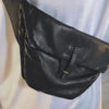 Person in a white shirt showing all of the features and pockets of a black leather crossbody belt bag