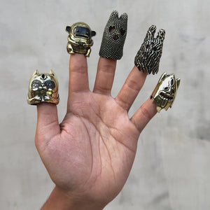 A hand displaying five unique finger puppets willing their fingers against a light gray background. Crafted in gold brass with black accents.