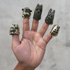 A hand displaying five unique finger puppets willing their fingers against a light gray background. Crafted in gold brass with black accents.