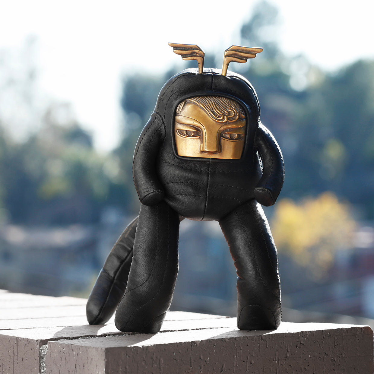 Black plush toy with gold head and wings on a stone ledge outdoors