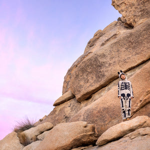 Person wearing a skeleton onesie standing on a rock with a rocky terrain and clear skies behind them