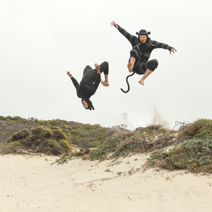 two people wearing animal onesies do tricks and flips off of a sand dune
