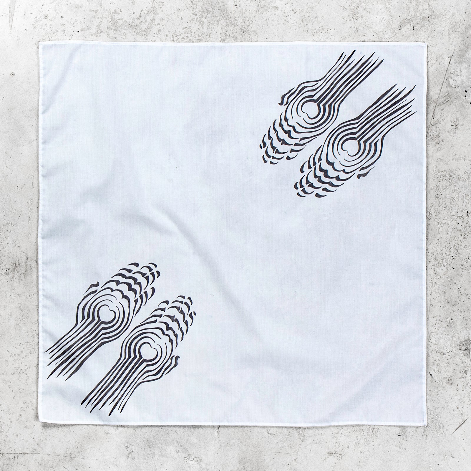 A square white fabric bandana featuring two black abstract spiral patterns, laid flat on a textured gray concrete surface.