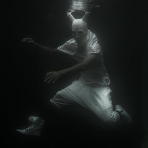 Person wearing all white clothing under water in a dark setting