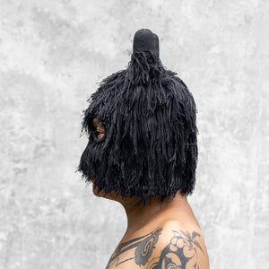 A man from the chest up facing sideways wearing a fuzzy black balaclava with horns that is covering half her face. 