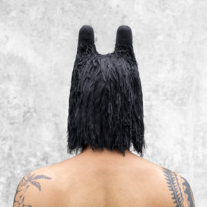 A man from the chest up facing back wearing a fuzzy black balaclava with horns that is covering half her face. 