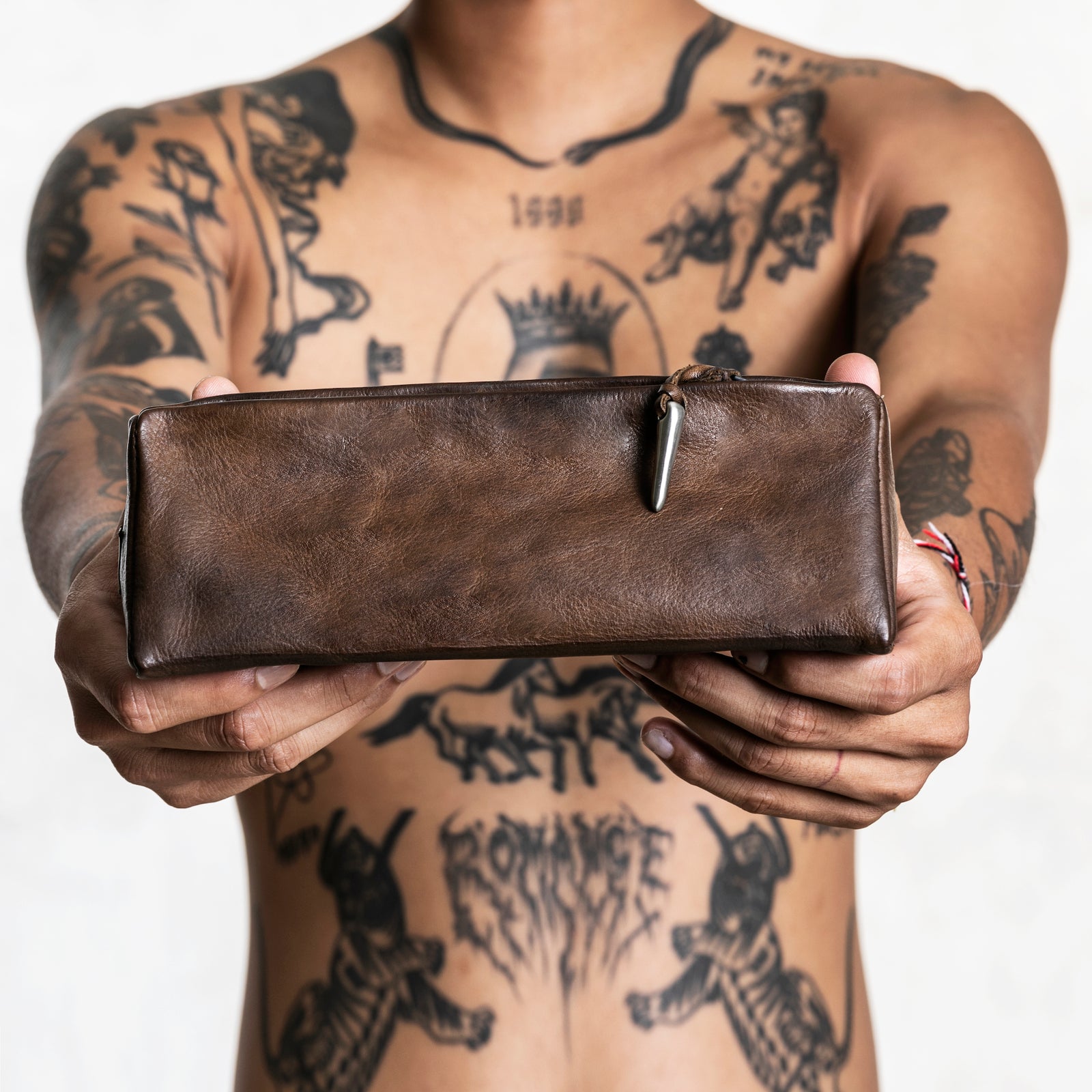 Shirtless tattooed person holding a brown leather pouch 
