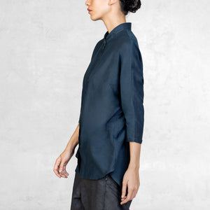 A woman standing from the waist up facing to the side wearing dark indigo pants and an Indigo Blue 3/4 sleeve cotton silk button up with an asian style collar