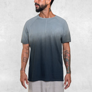 Man standing from the waist up wearing a short sleeve cotton tee shirt that fades from indigo blue at the hem toward light blue at the shoulders