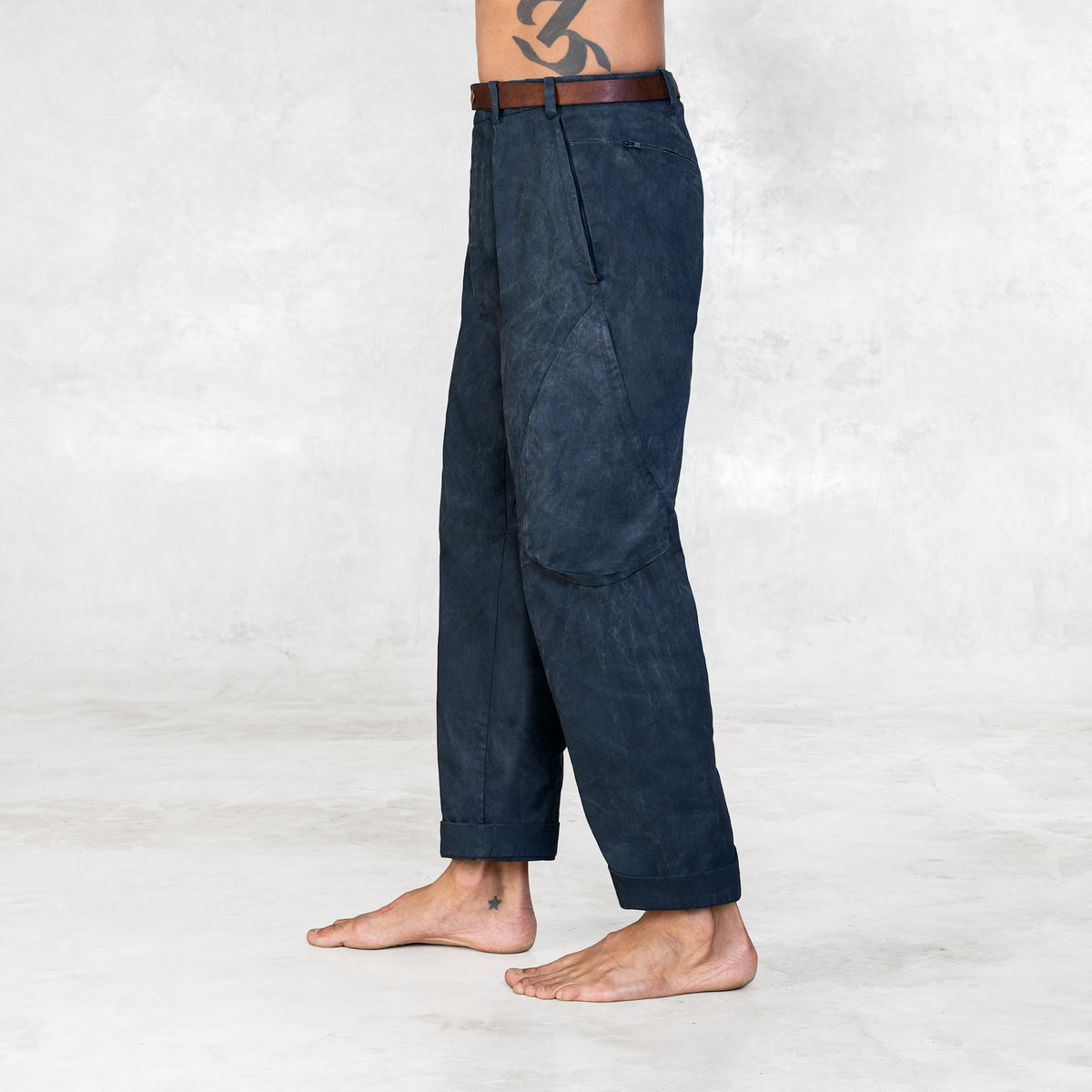 A man facing sideways wearing Indigo colored twill cotton cargo-style pants with a brown leather belt.  Shown from foot to waist.