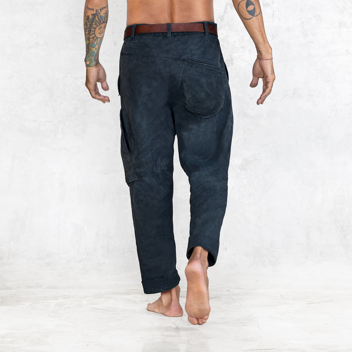 A man facing back wearing Indigo colored twill cotton cargo-style pants with a brown leather belt. Shown from foot to waist.