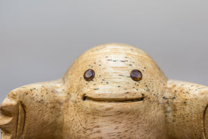 Small wooden sculpture with arms extended in a HUG position and smoky quartz gem eyes close up