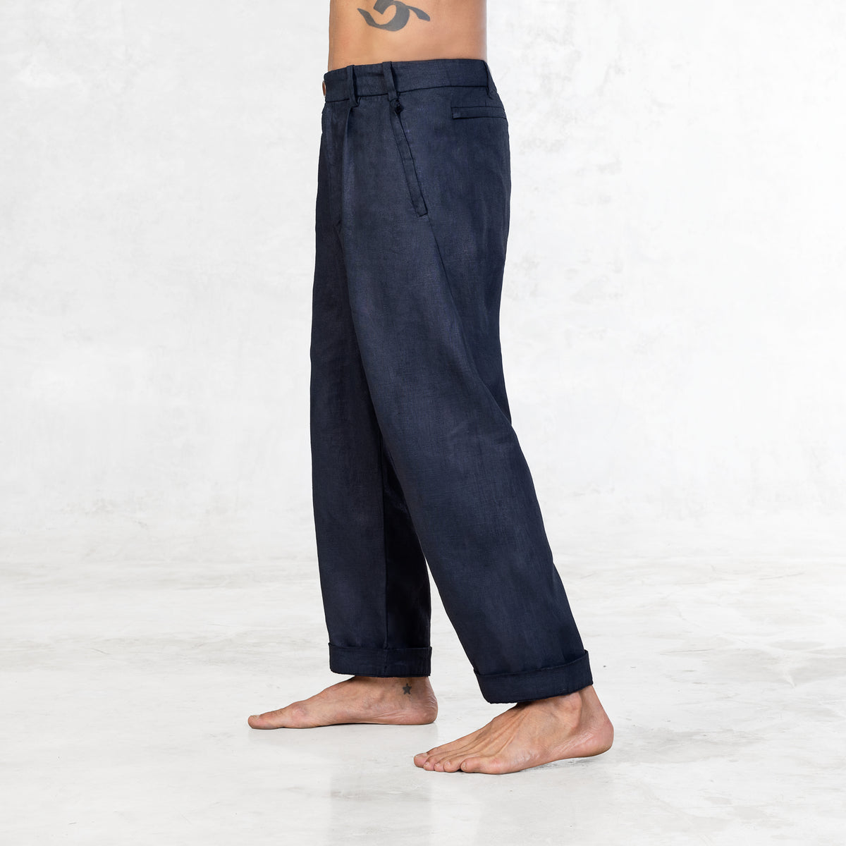 A shirtless man standing facing side from the waist down wearing Indigo blue linen pants