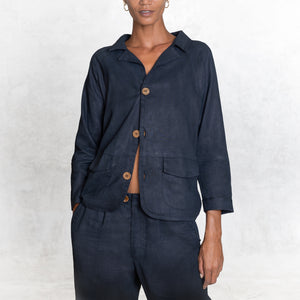 A woman standing facing front from the thighs up wearing an Indigo Blue Linen suit. A 3 button button-up jacket with 3/4 sleeves.