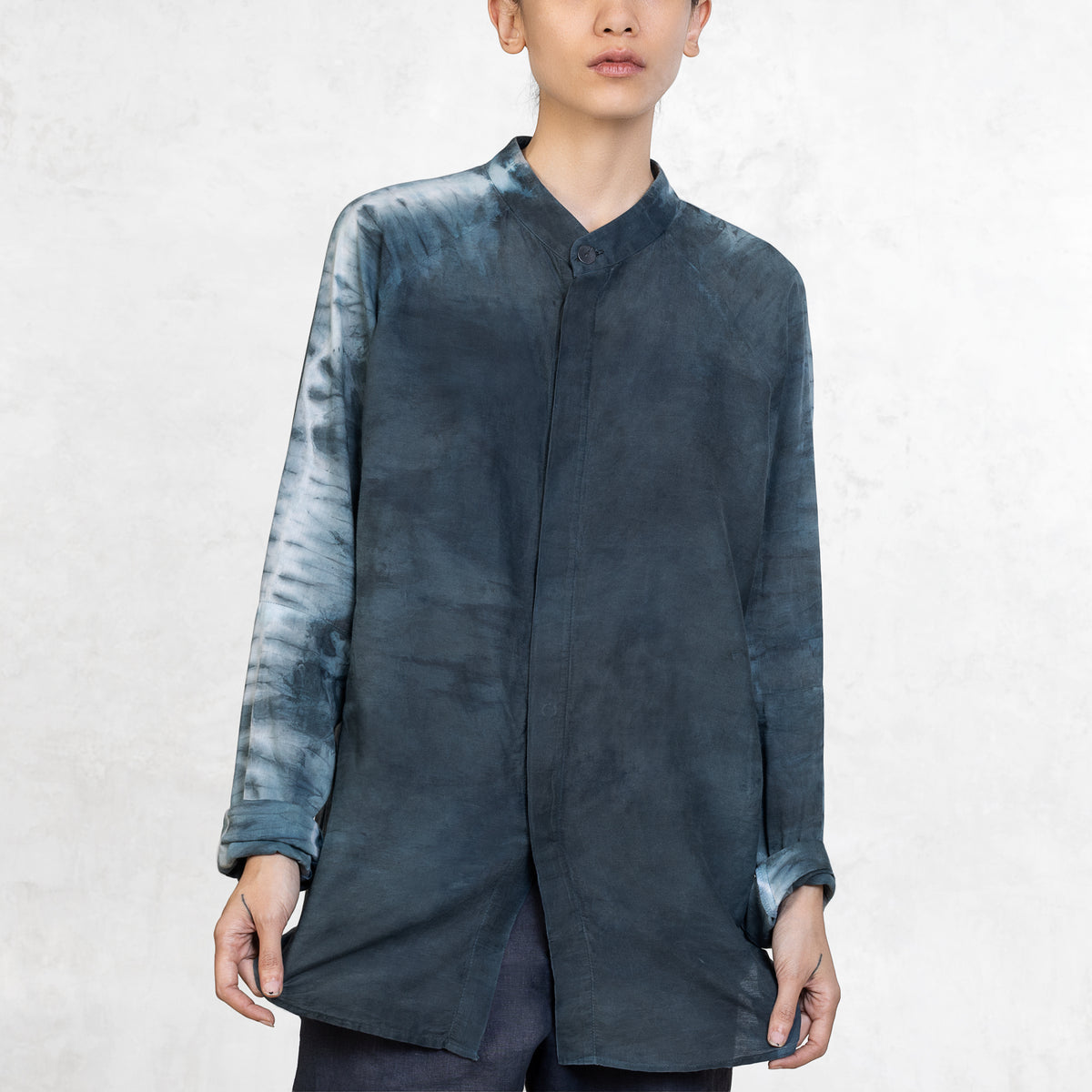A woman standing from the waist up facing front wearing dark indigo pants and a light Indigo Blue long sleeve cotton silk button up with tie dyed arms