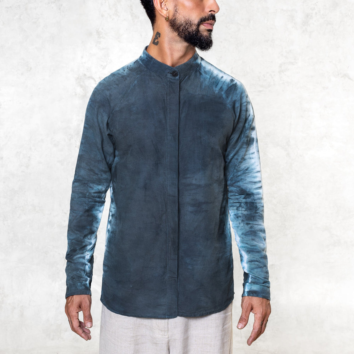 A man standing from the waist up facing front wearing white pants and an Indigo Blue long sleeve cotton silk button up with tie dyed arms