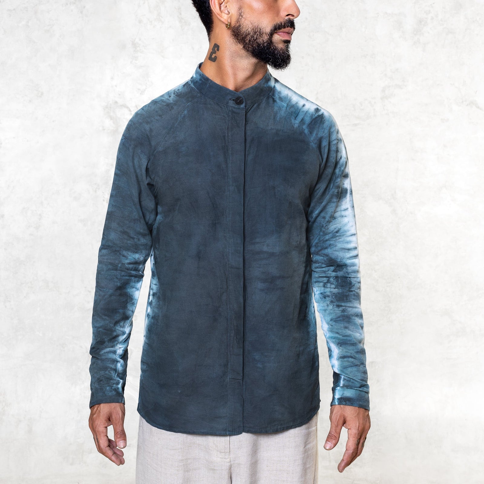 A man standing from the waist up facing front wearing white pants and an Indigo Blue long sleeve cotton silk button up with tie dyed arms