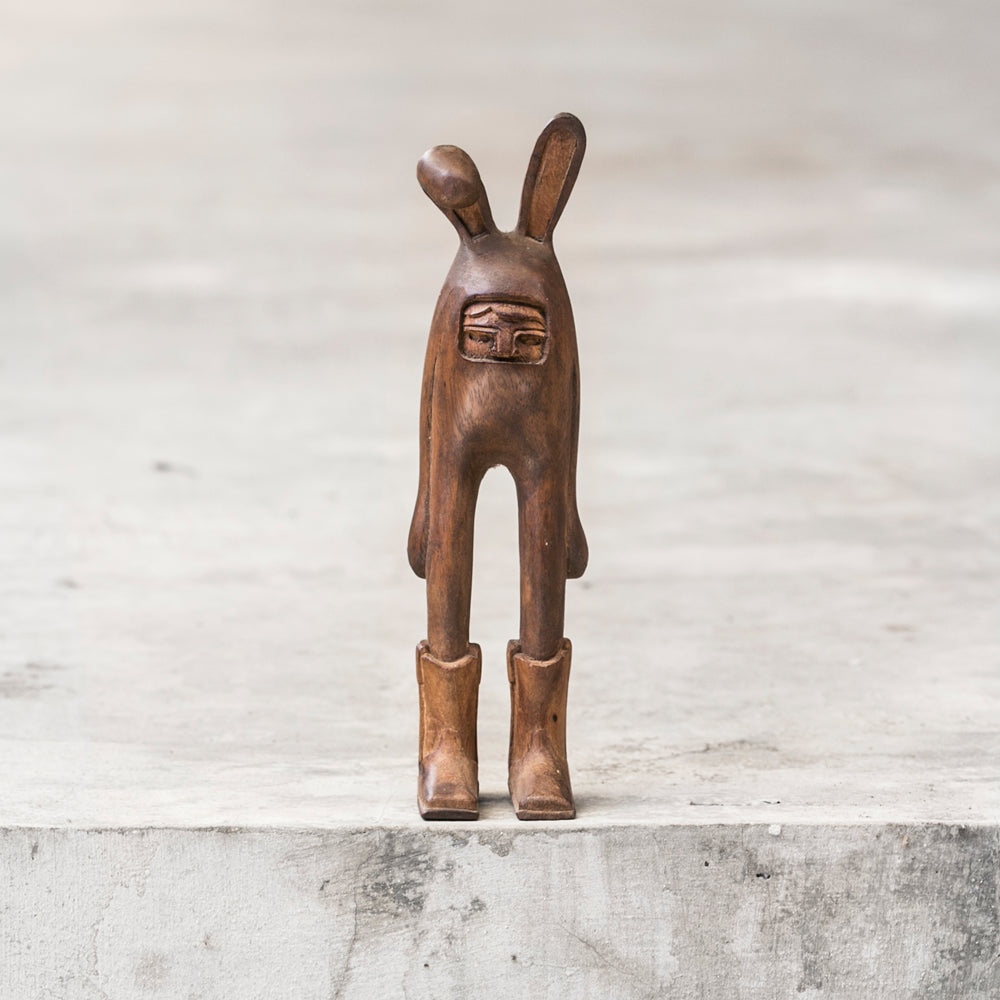 Small brown wooden rabbit sculpture  wearing cowboy boots standing on a gray ledge