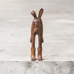 Small brown wooden rabbit sculpture  wearing cowboy boots standing on a gray ledge
