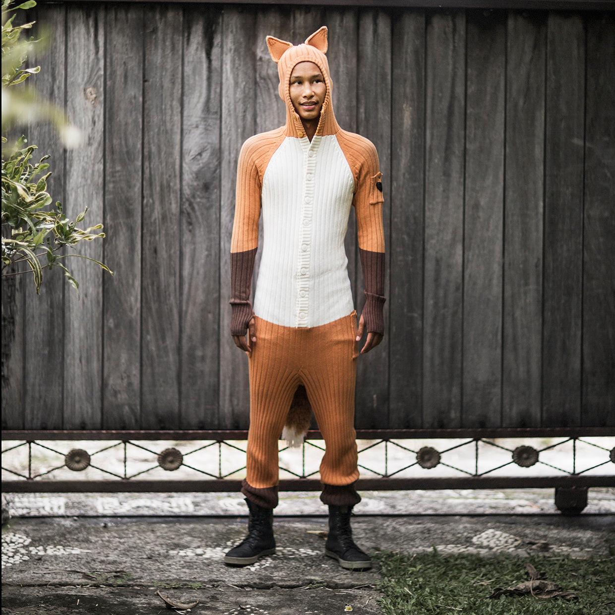 Person wearing a hooded knit orange fox onesie costume against a gray background