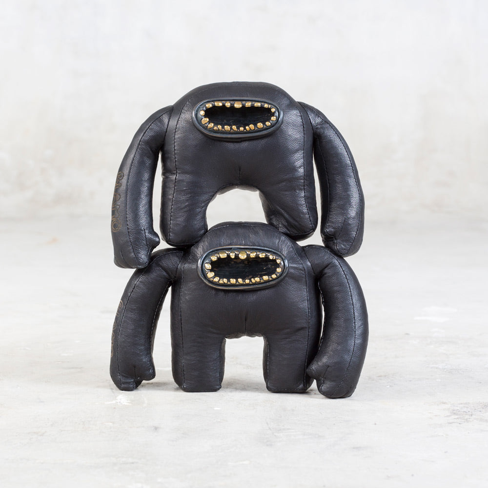 Two black leather toys with a large open mouth with brass teeth set against a neutral background.