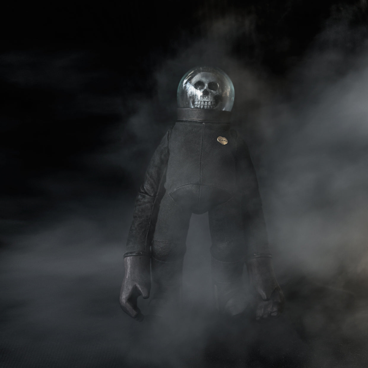 Leather, suede, glass, and wooden skull spaceman figurine standing in a smoky setting against a black background